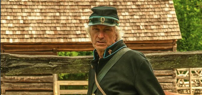 Patrick Minges in Civil War-era uniform at a historic log cabin